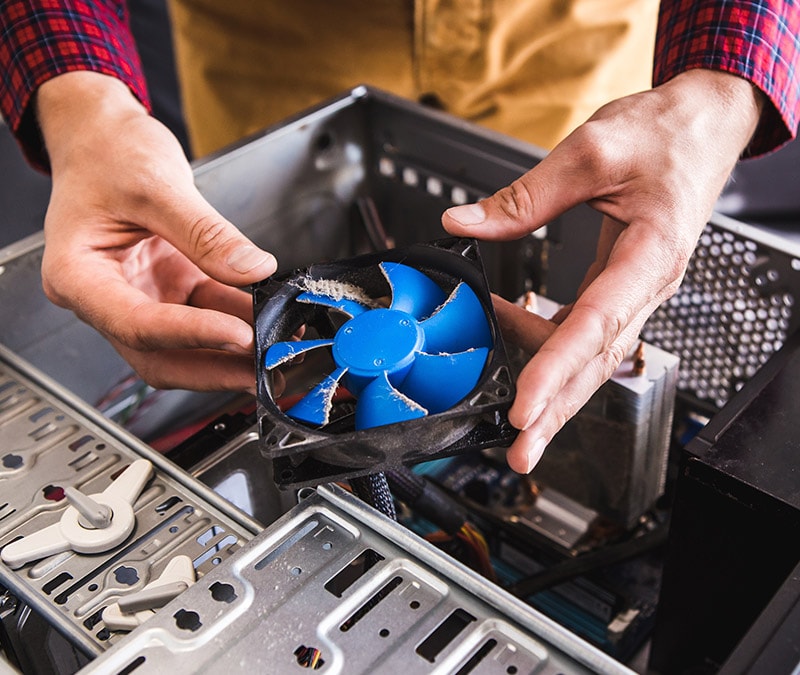 Close-up of hands removing dust from a computer fan, demonstrating how to clean a PC.